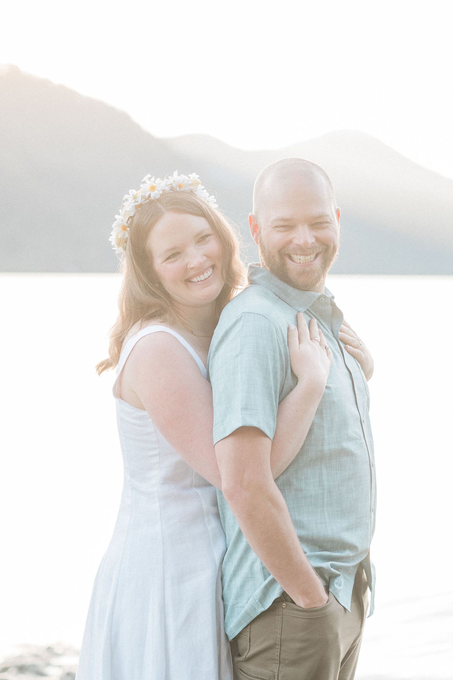 bride hugs groom from behind with sunrise light falling on them during their Washington elopement