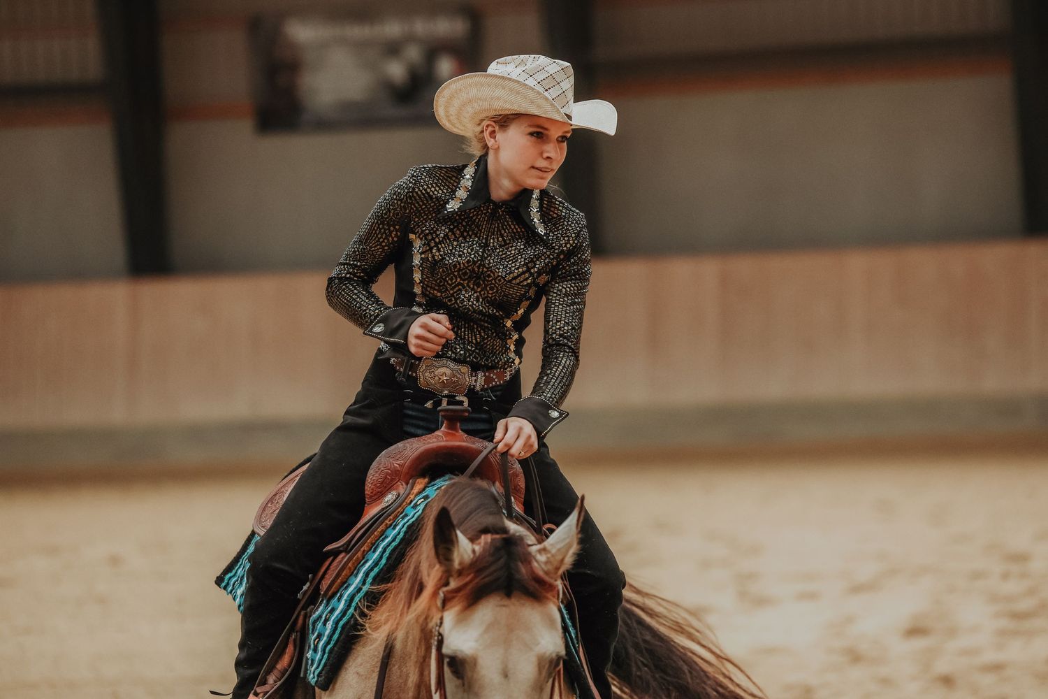 Rider in western attire performs on a paint horse during an indoor competition.