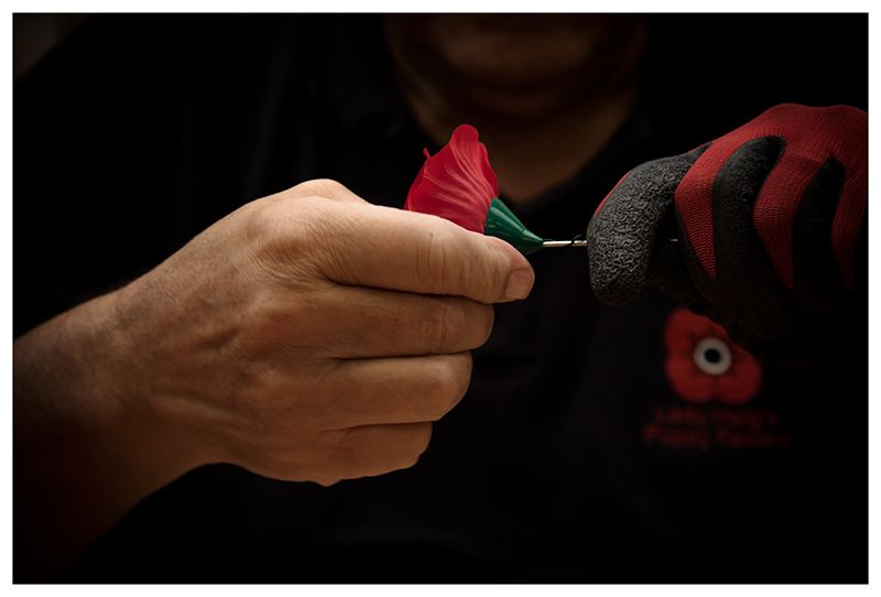 Close-up of hands working on a red and black craft project with a needle.
