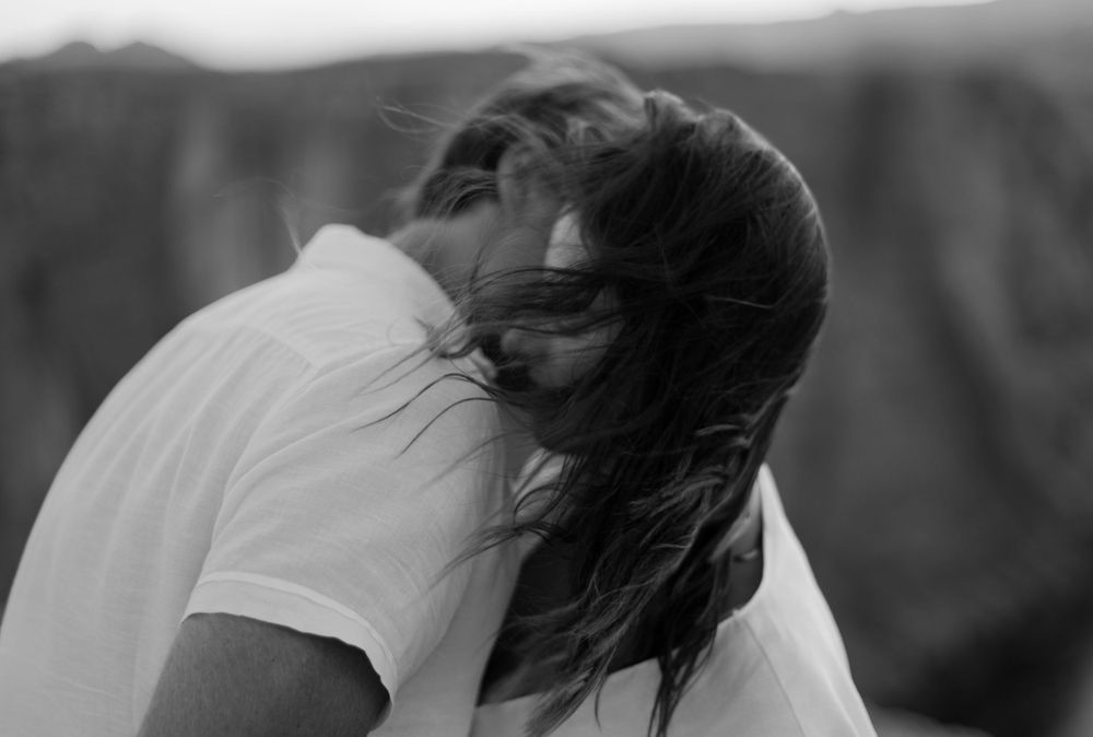 Black and white profile shot of couple embracing with wind-blown hair against canyon backdrop.
