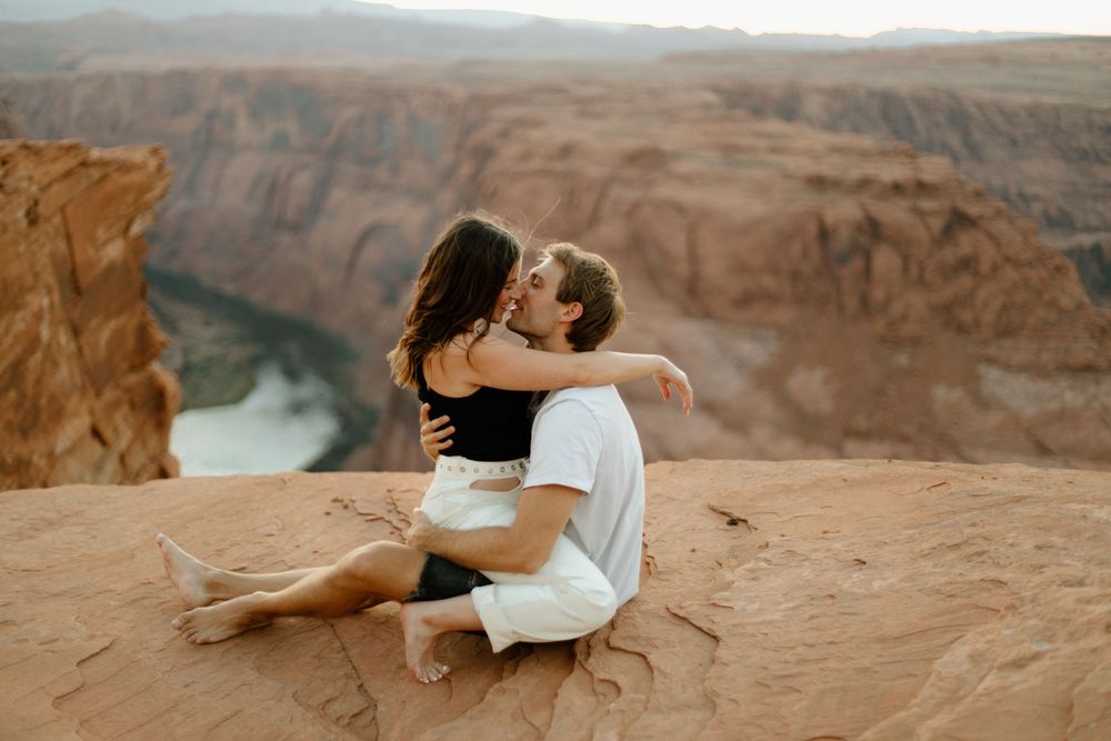 Couple sharing tender moment on red rock outcrop with scenic river canyon view.