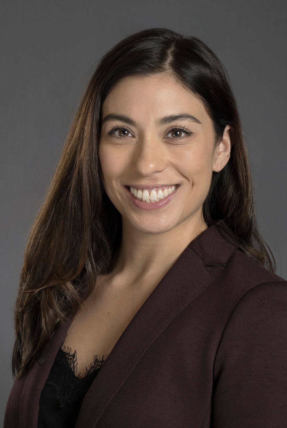Smiling woman with dark hair wearing a burgundy blazer poses for a professional headshot.