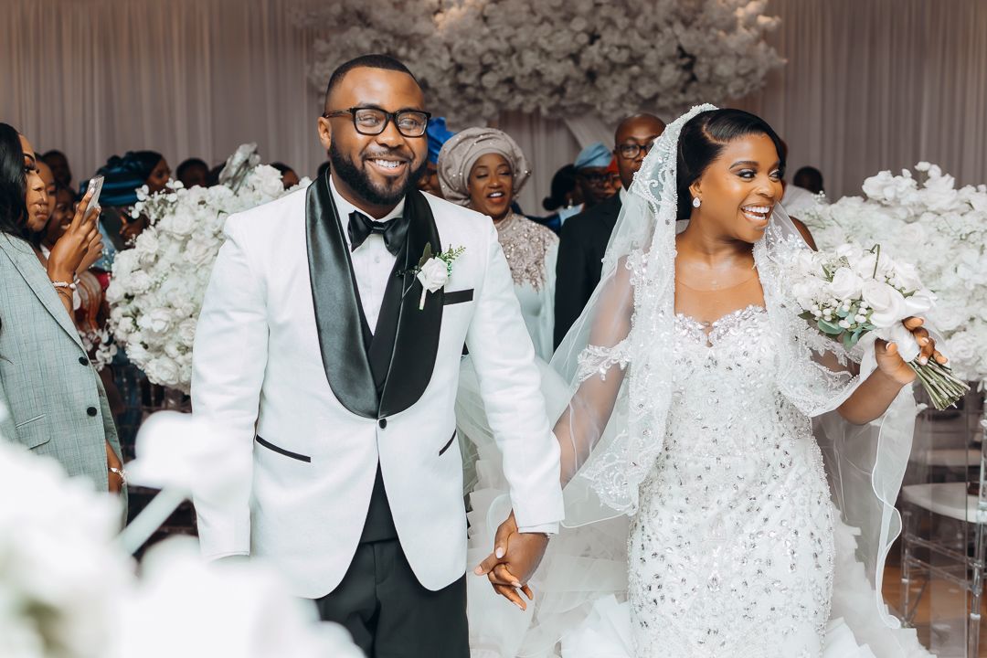 Joyful wedding couple celebrating in white attire surrounded by floral decorations.