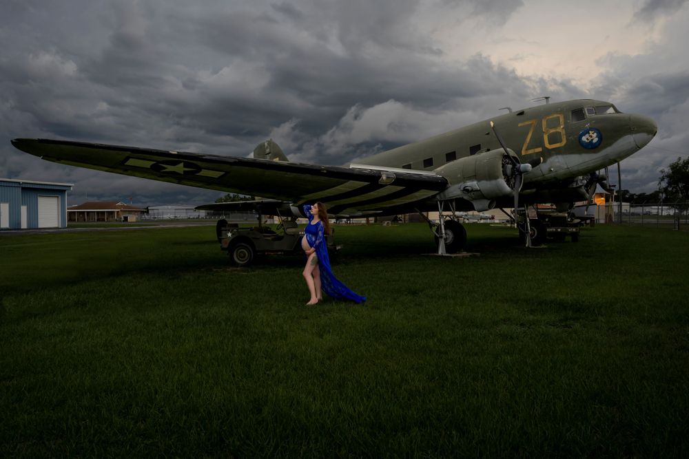 Vintage aircraft on grassy field under dramatic stormy sky at sunset.