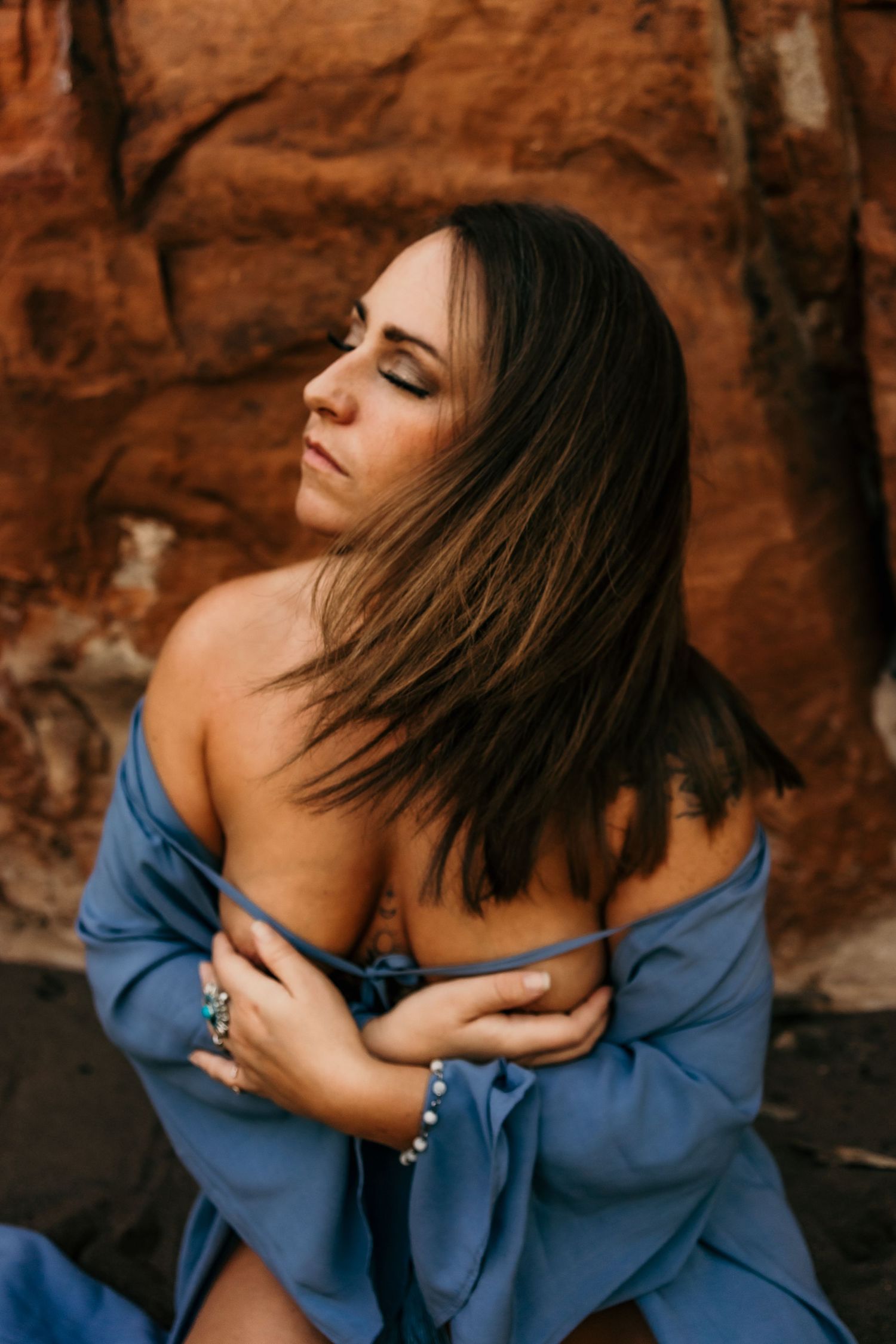 Artistic portrait with blue clothing against textured red rock wall.