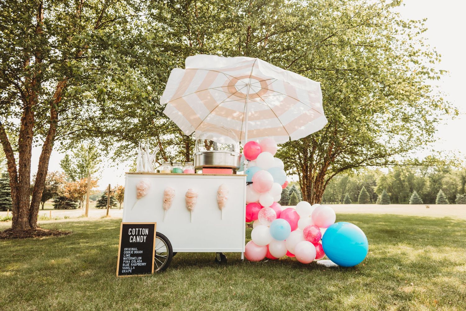 Outdoor party setup with colorful balloons and white tent under trees.