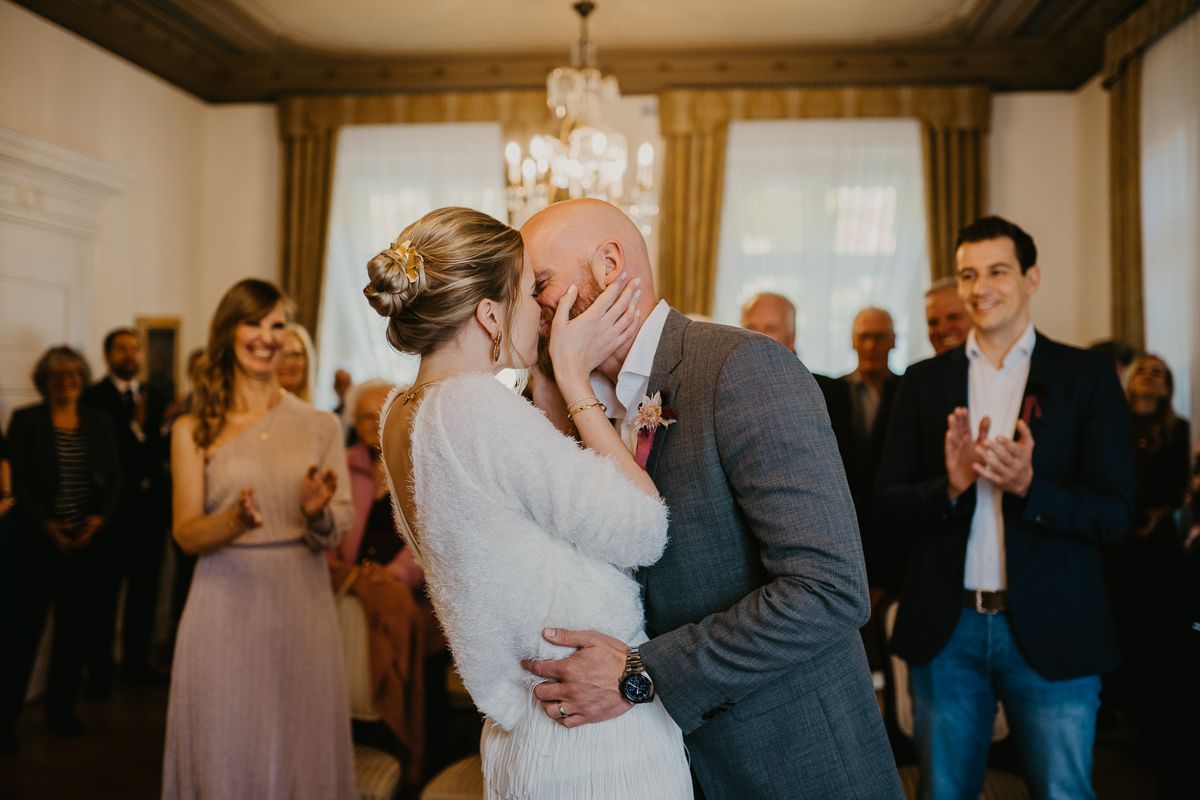 Intimate wedding moment with guests applauding in an elegant room with chandelier.
