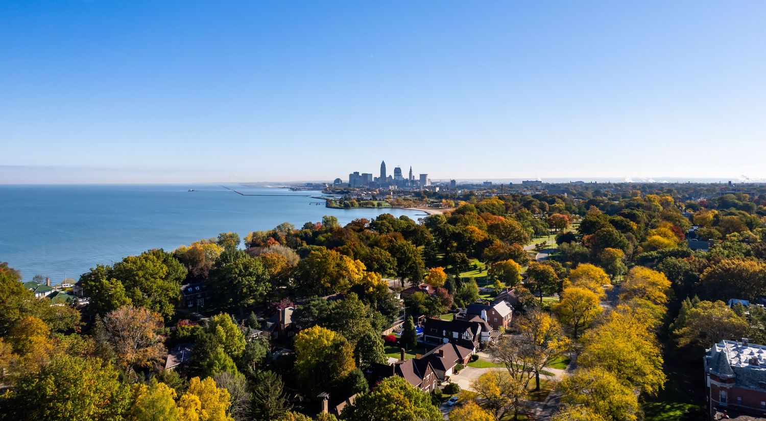 Panoramic autumn view of Cleveland skyline across Lake Erie with colorful fall foliage in foreground.