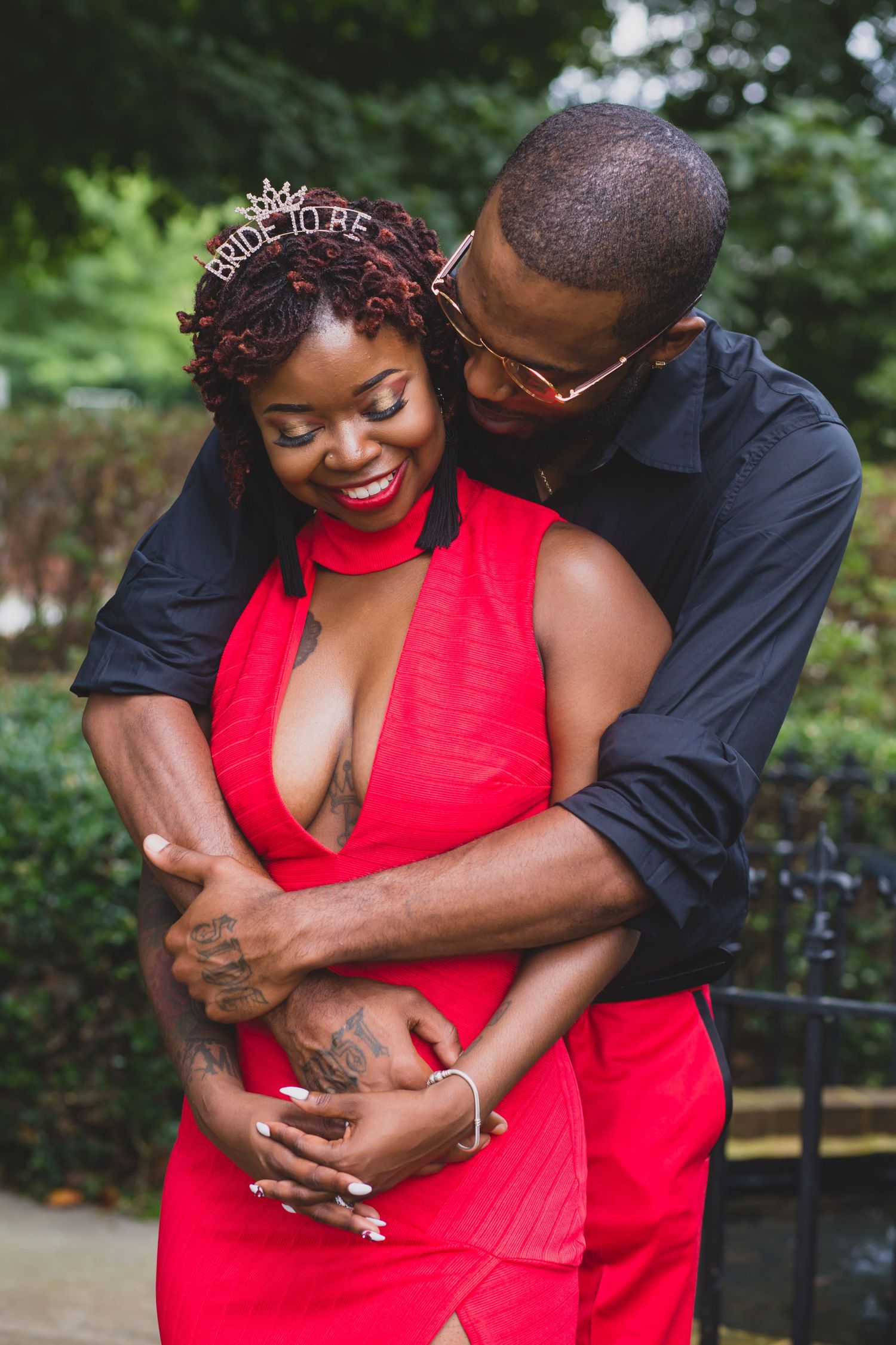 Romantic couple embracing outdoors, with woman in red dress and man in dark shirt.
