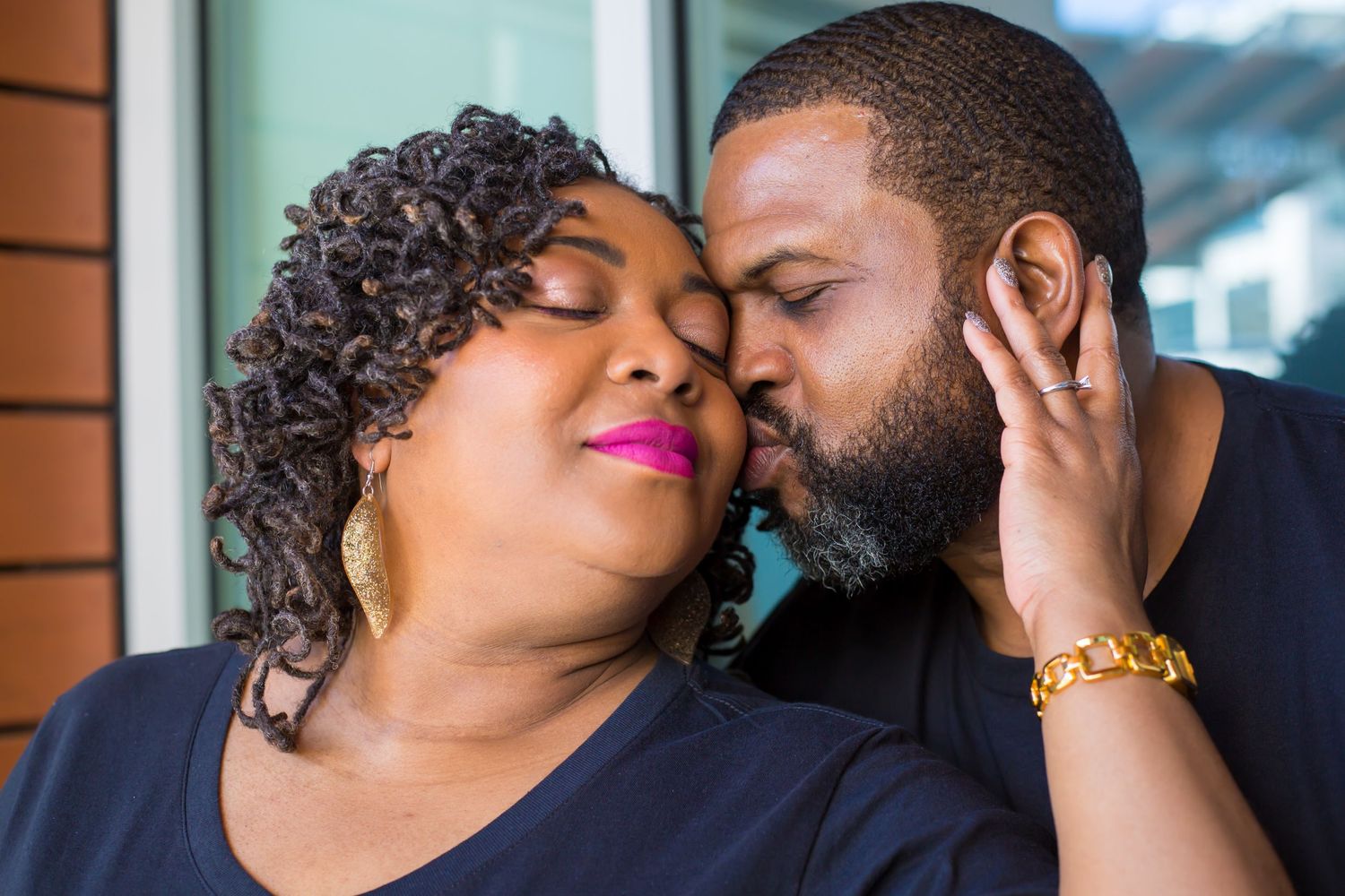 Intimate couple sharing a tender romantic moment together against a brick wall exterior.