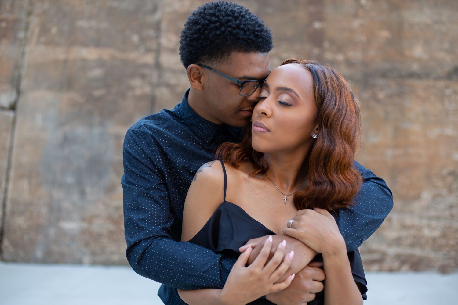 A romantic couple embraces against a rustic brick wall background.