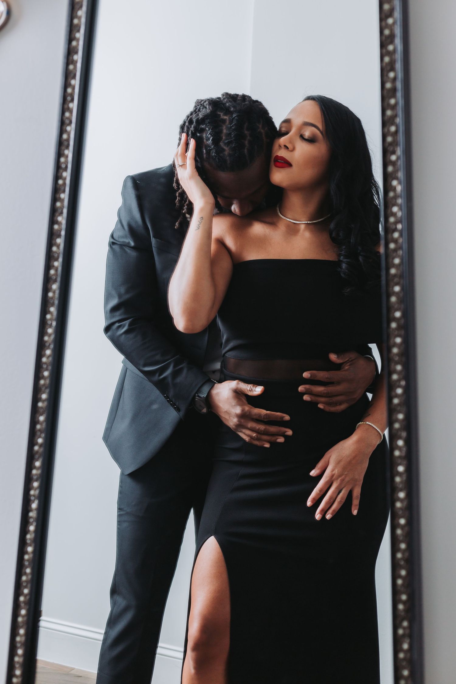 Intimate couple portrait in formal wear against mirror during photoshoot.