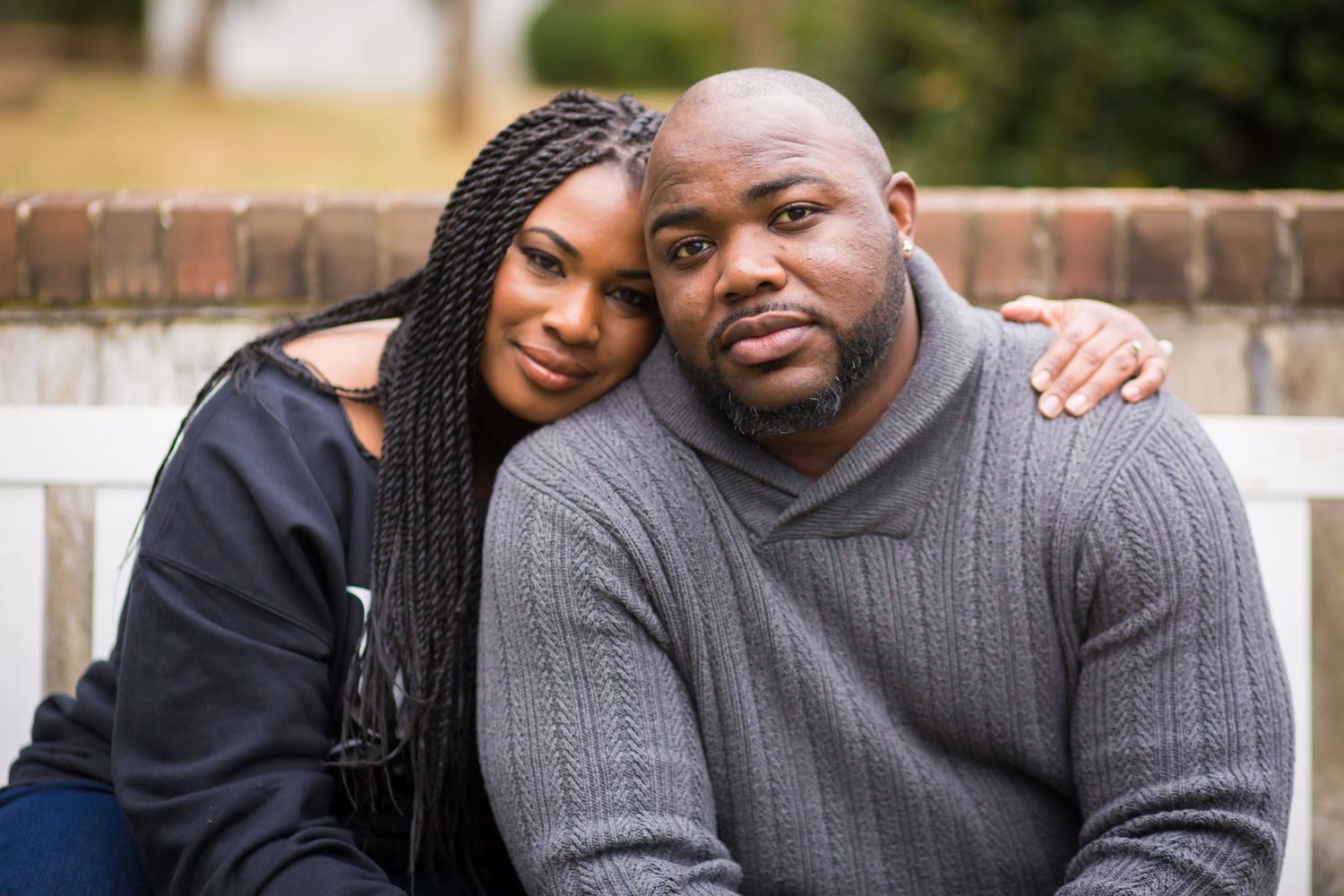 Loving couple shares intimate outdoor portrait while smiling at the camera in casual sweaters.
