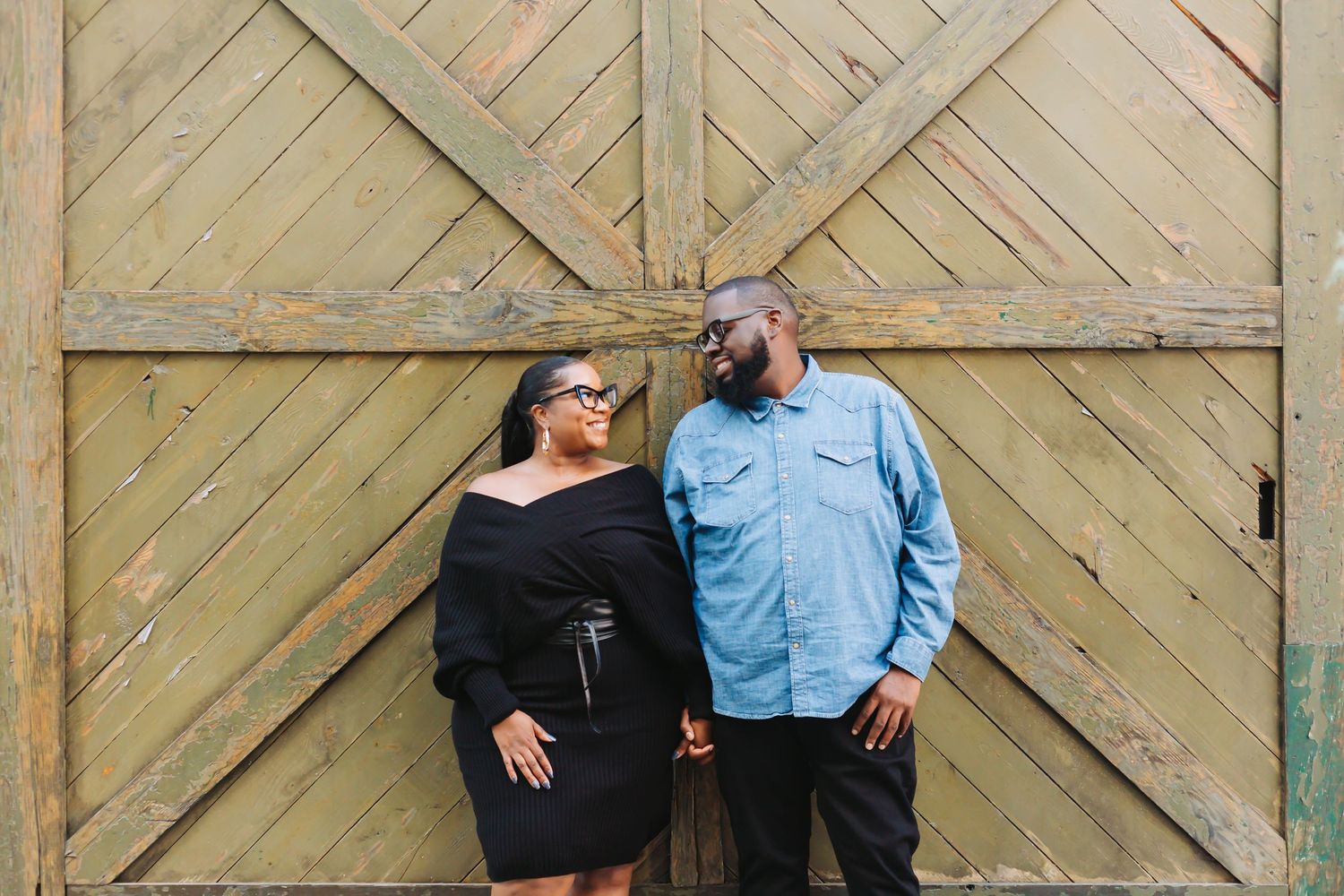 Couple poses playfully in front of rustic wooden barn doors.