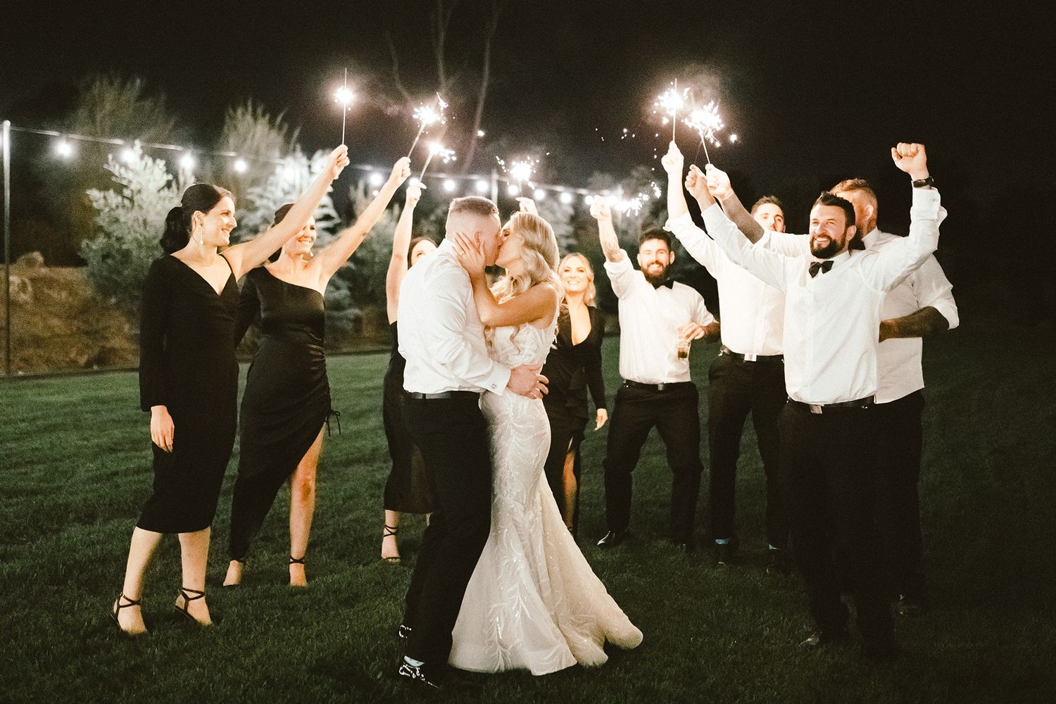Wedding party celebrates with sparklers at night during an outdoor reception.