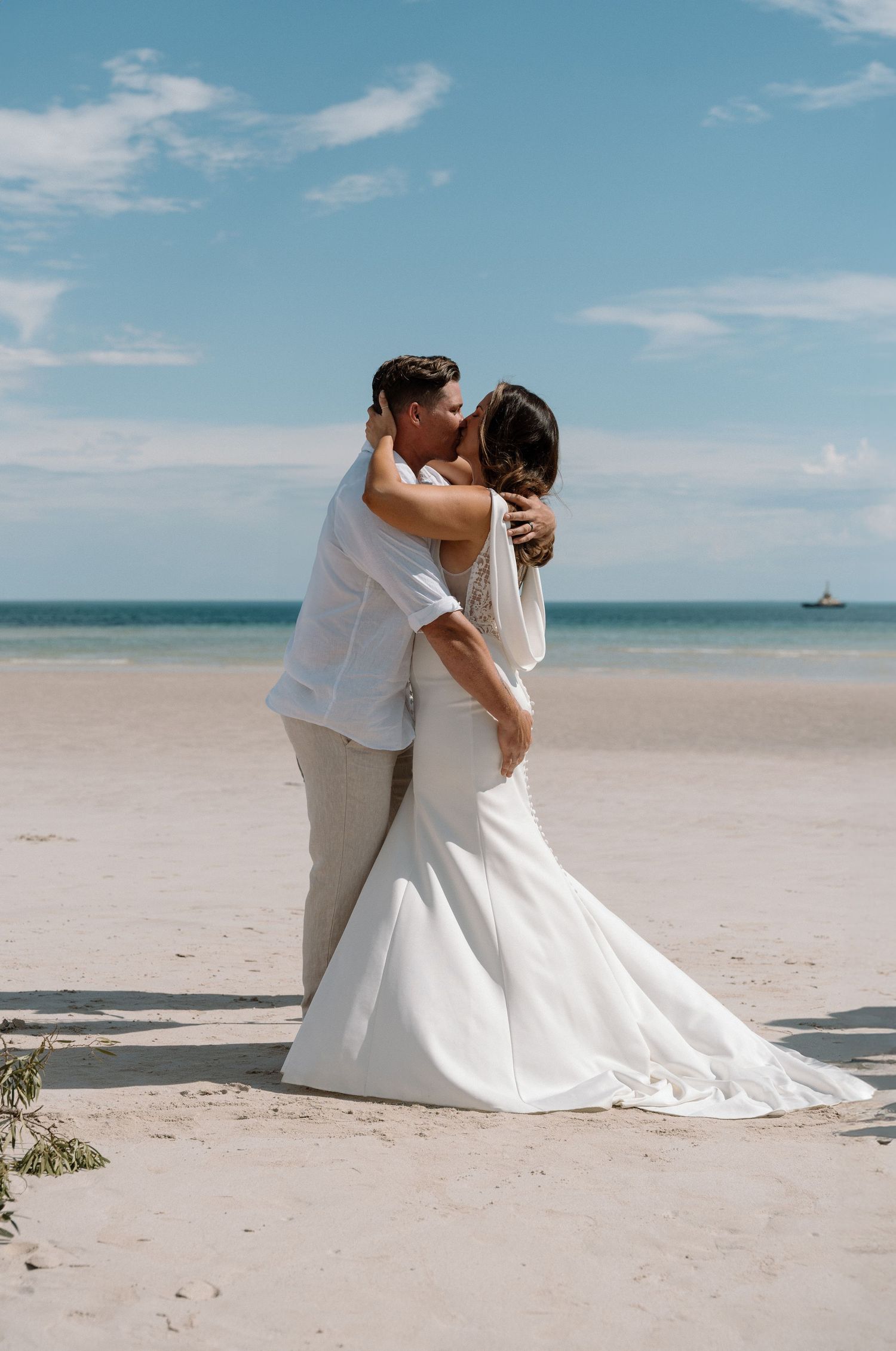 Romantic beach wedding photoshoot with couple embracing on sandy shore.