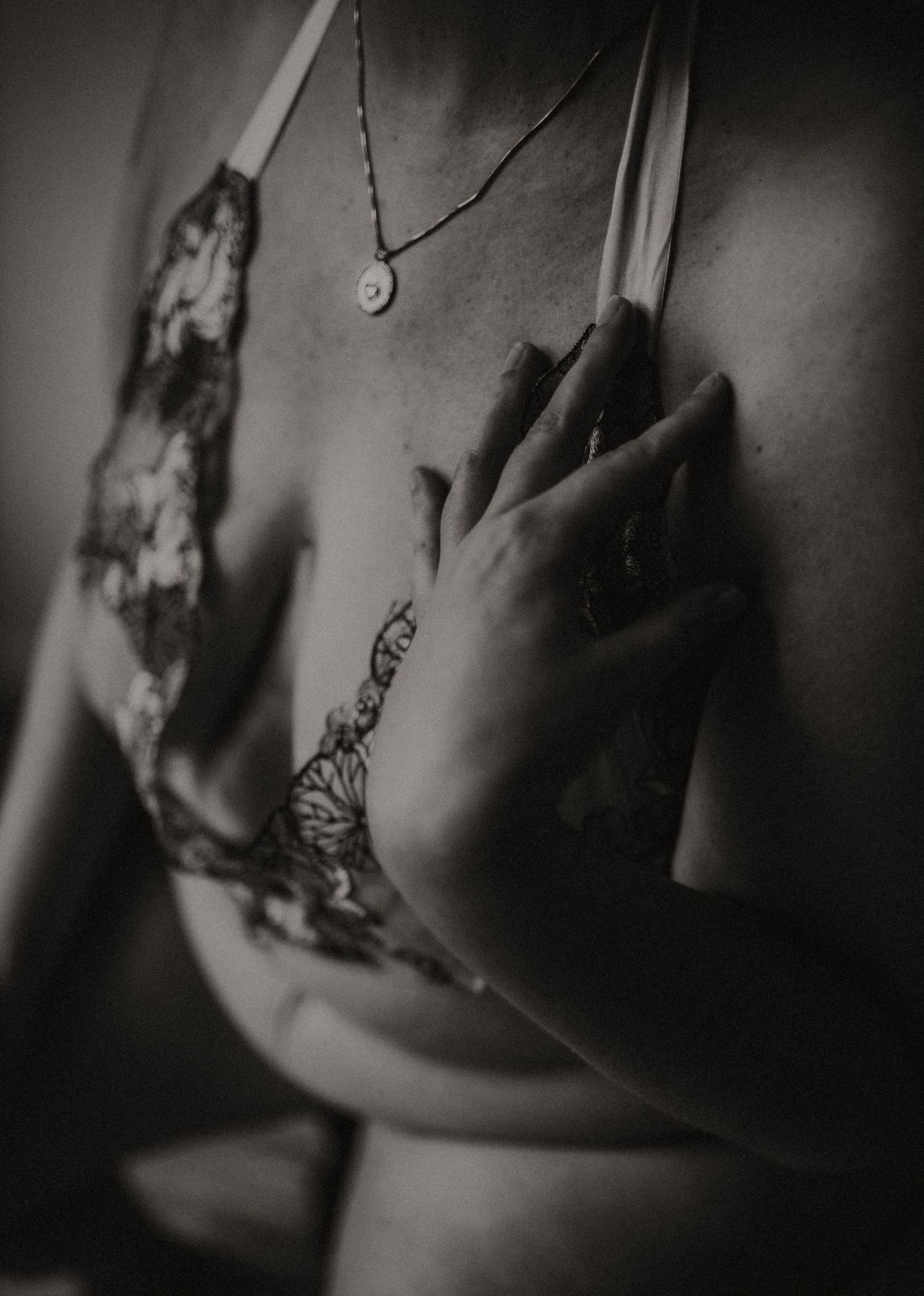 Black and white artistic photograph showing hands with delicate lace lingerie designs and a necklace pendant.