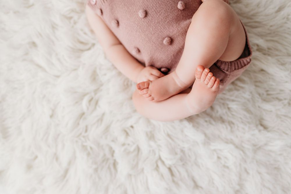 Adorable newborn baby feet resting on soft white fur blanket with pink and white tones.