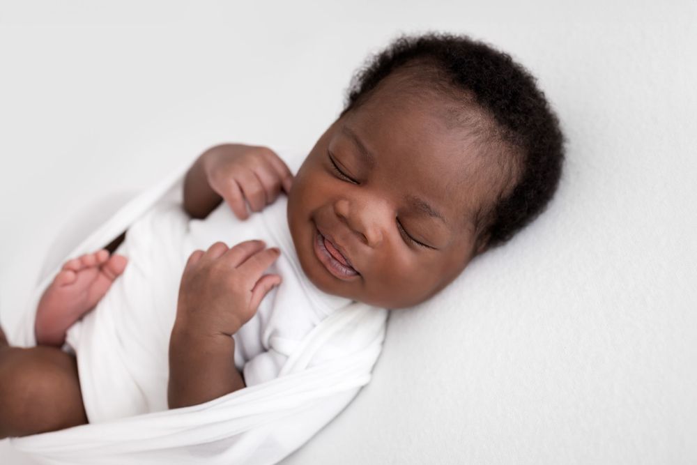 A sweet newborn baby in swaddle sleeping with a smile against a white backdrop