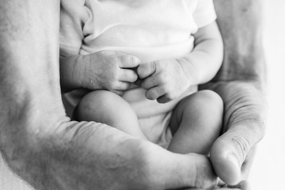 A tender black and white close-up of tiny baby feet being gently cradled in adult hands.