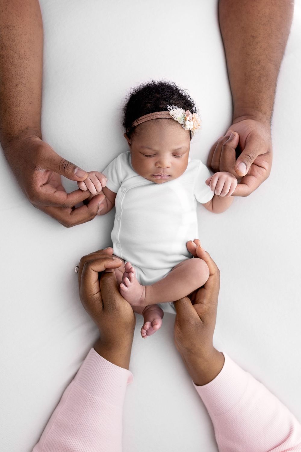 Newborn baby girl with cute floral headband holding dads hands and moms hands cradling newborn in Santa Fe newborn photography studio in NM
