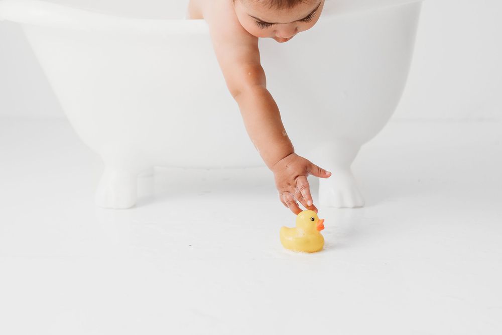 Baby reaching for rubber duck from baby bubble bath after cake smash in Santa Fe NM baby studio.