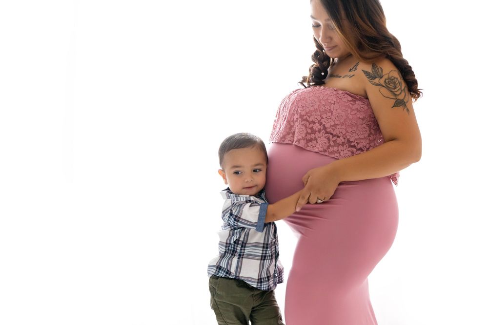 Toddler little boy hugging pregnant mom's belly. Mom wearing a pink maternity gown provided by Blooming Desert Photography. Mom and toddler