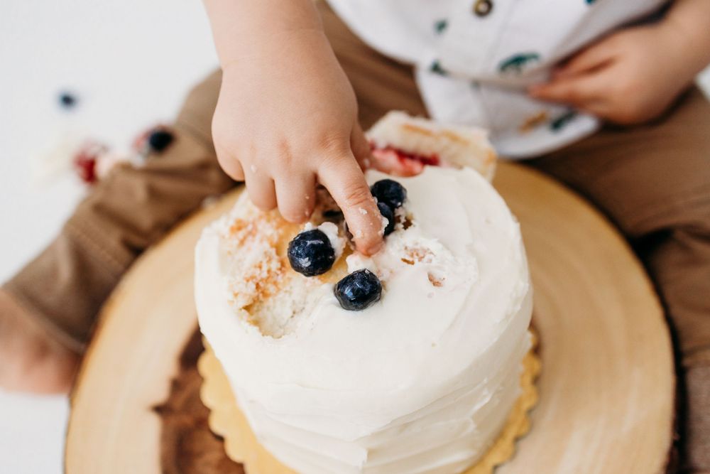 Detail photo of little baby toddler one year old hands pinching berries off his cake during cake smash session at Blooming Desert Photograph
