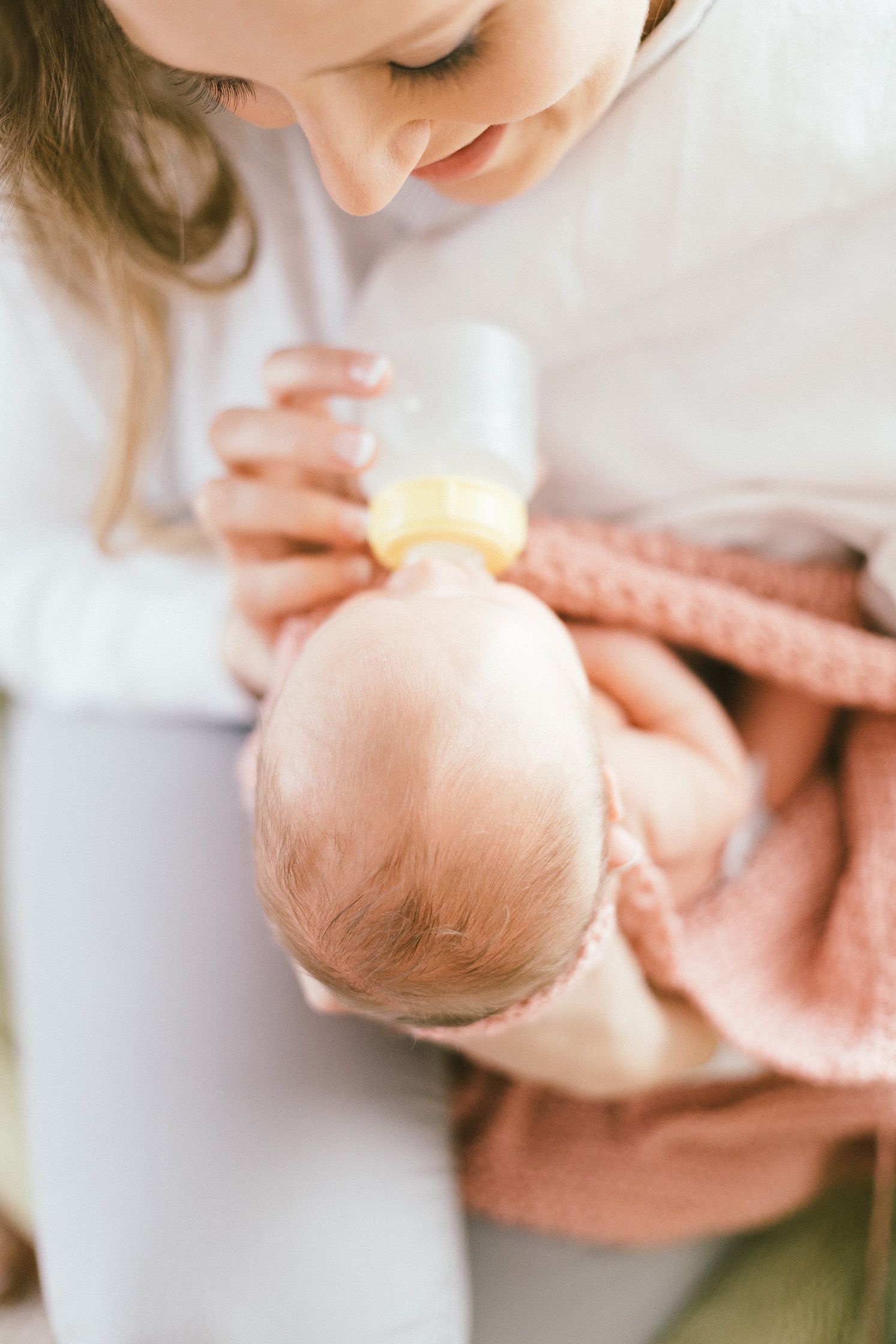 Overhead view of feeding time as caregiver gives bottle to infant wrapped in pink knit blanket.