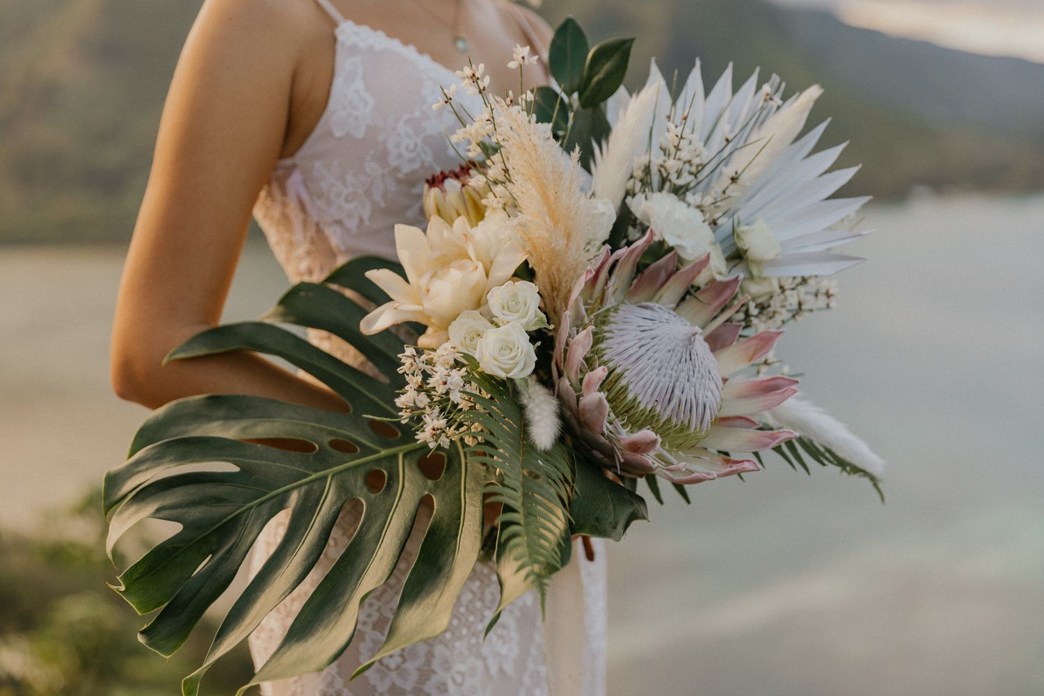 Close-up shots of elegant tropical wedding bouquets featuring white flowers, palm leaves and delicate greenery at sunset.