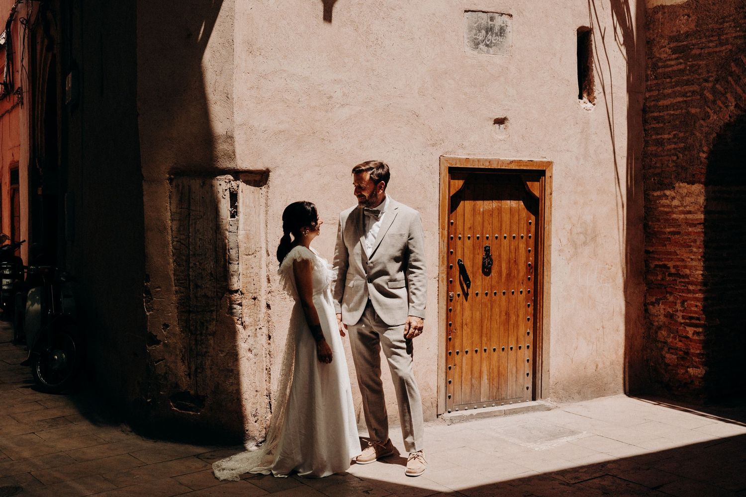 A couple shares an intimate moment in traditional wedding attire against a white stone wall.