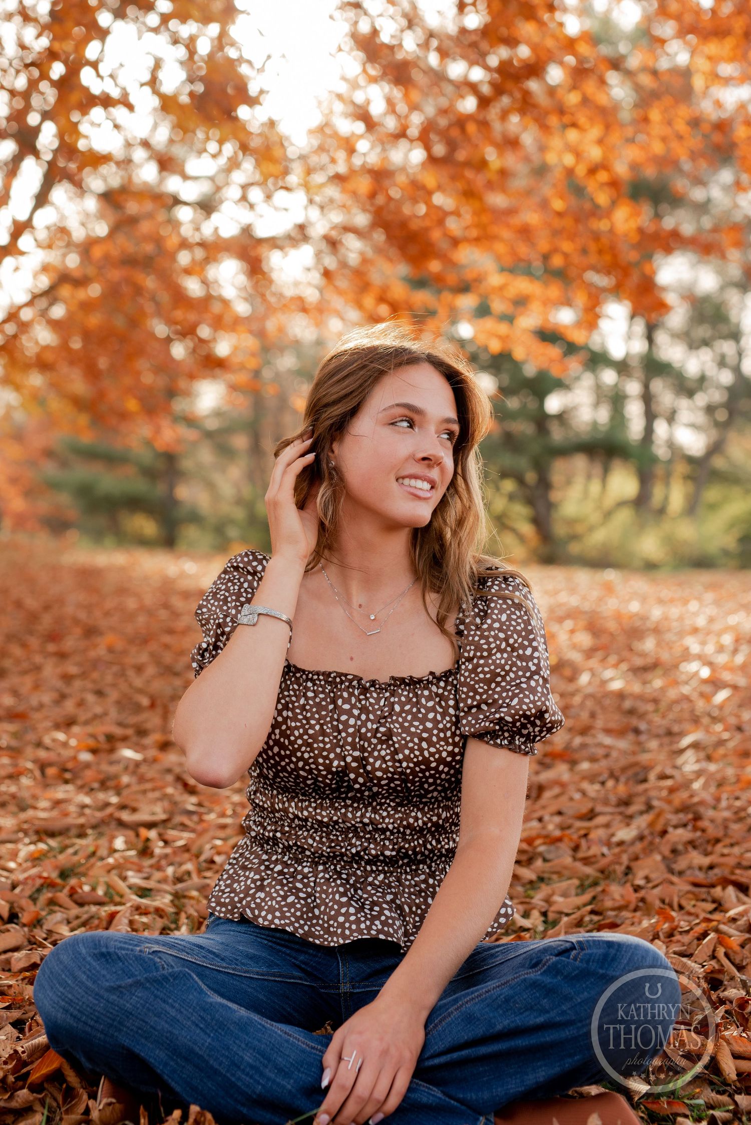 A casual autumn portrait sitting among fallen leaves wearing a leopard print top.