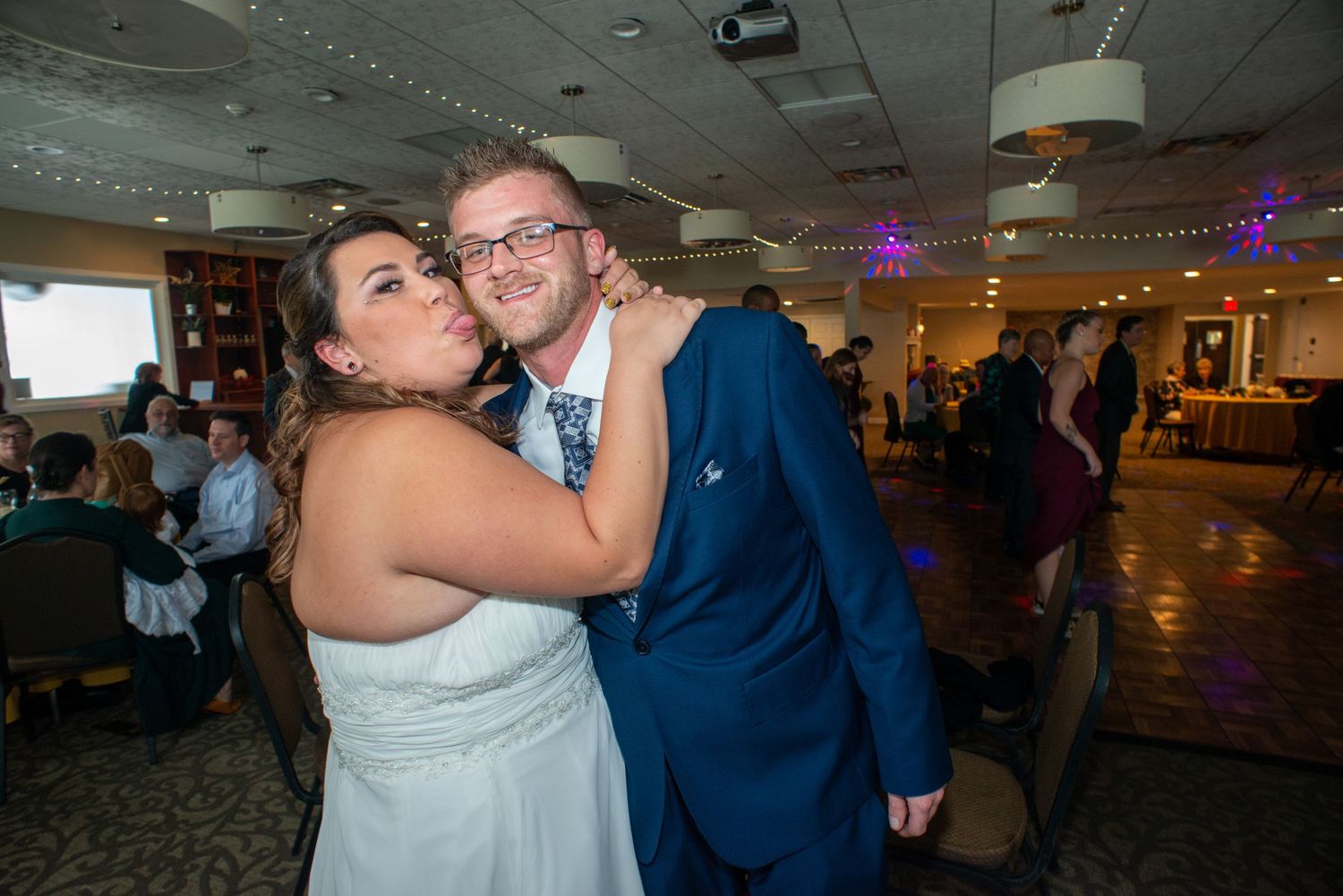 Joyful couple dancing together at their wedding reception in a venue with purple accent lighting.