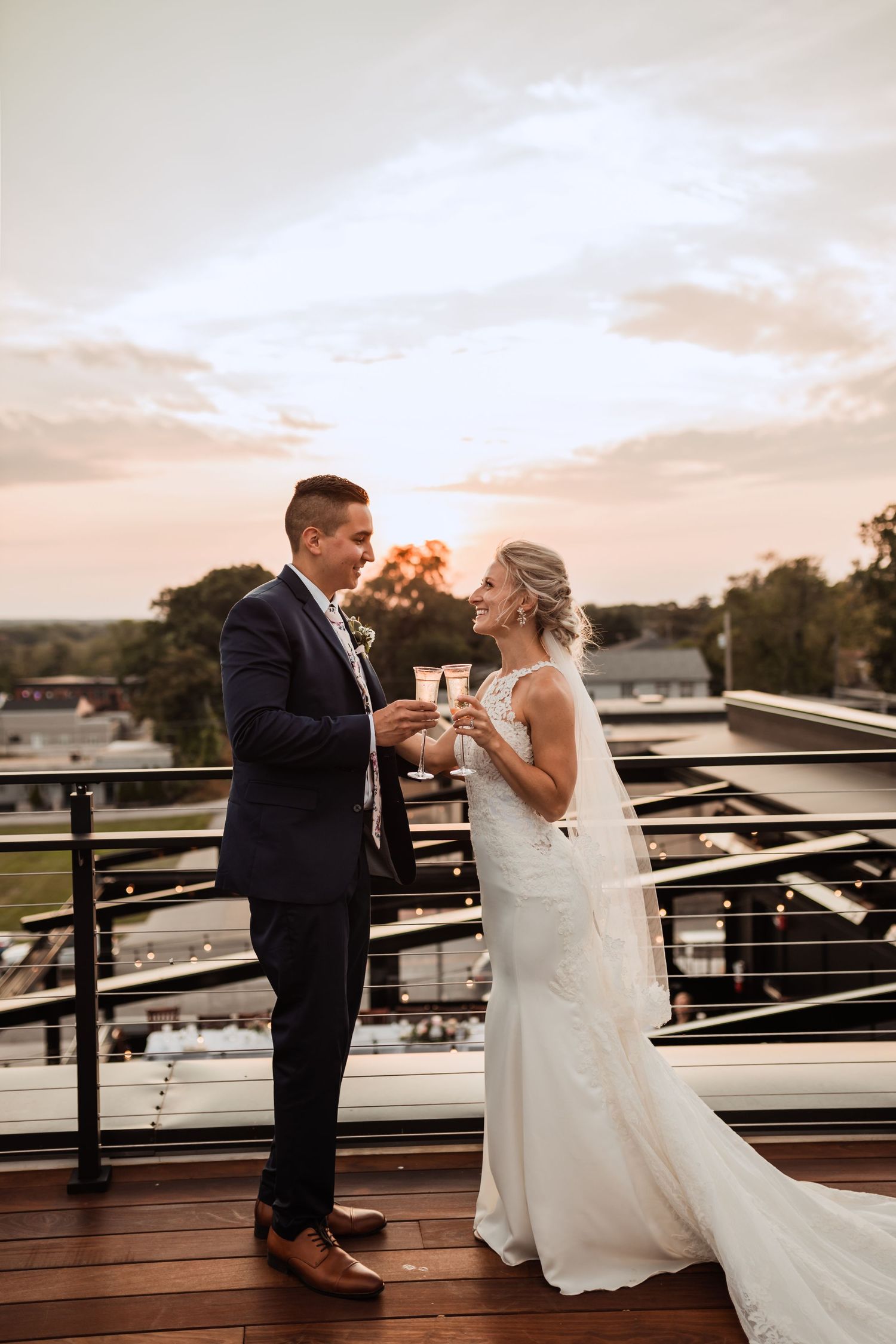 Newlyweds sharing champagne toast on rooftop deck at sunset.