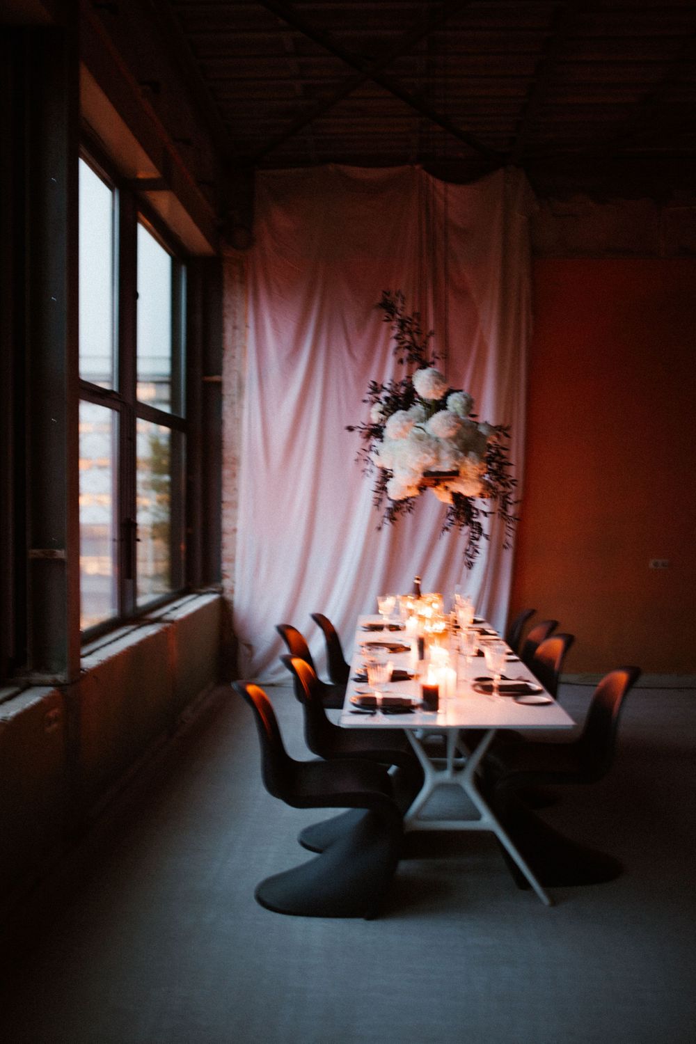 Modern dining space with white backdrop, floral arrangements and candlelit table settings.