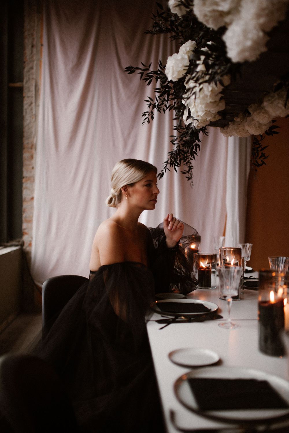 Moody table setting with white floral arrangements and candlelight against a draped white backdrop.