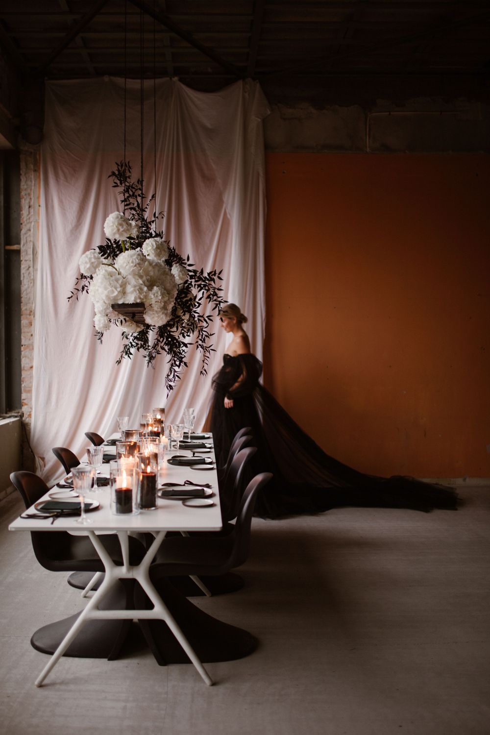 Candlelit table setting with white draping and floral arrangements in moody lighting.