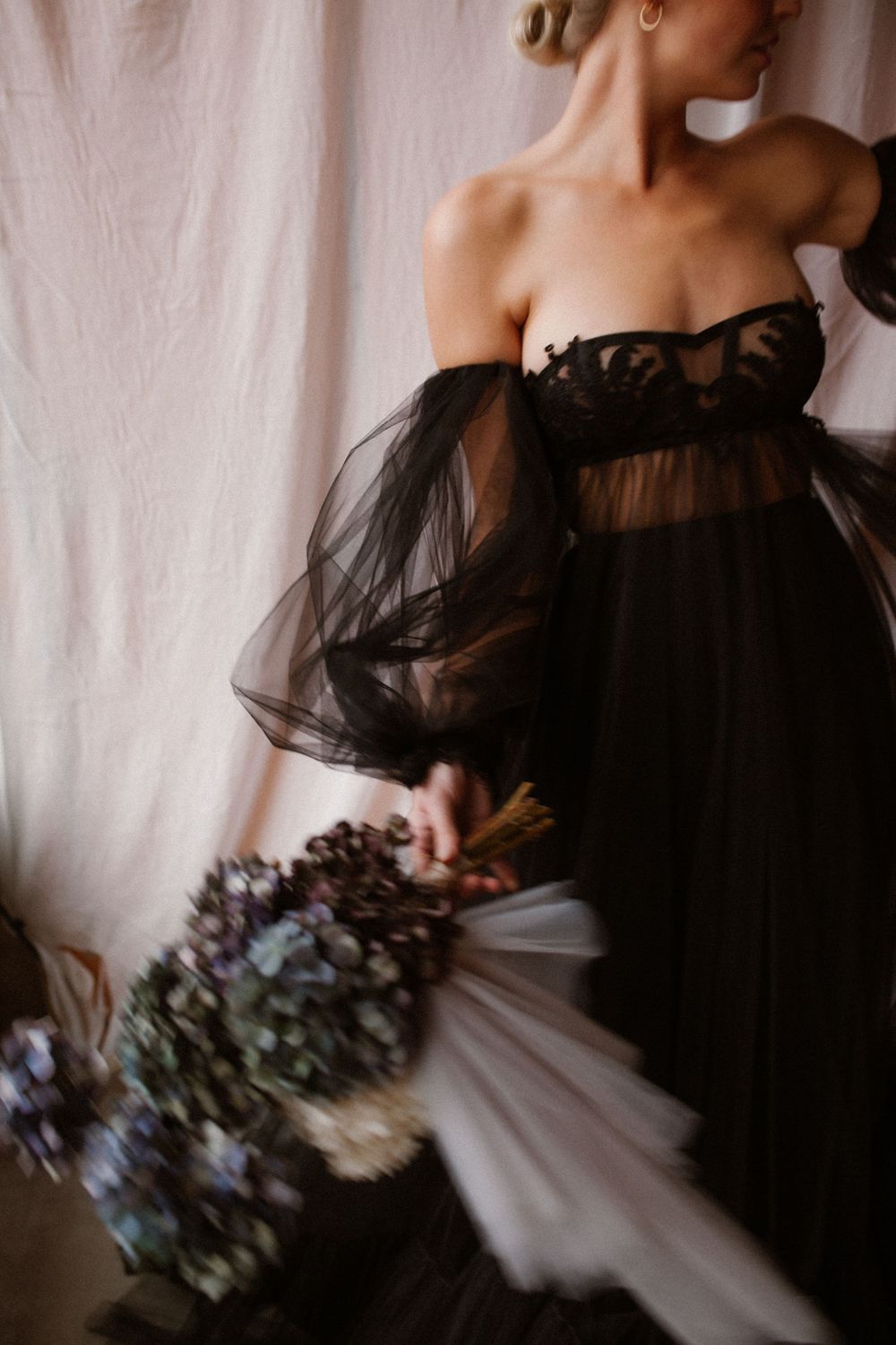Figure in black off-shoulder dress holding a bouquet of blue and purple flowers.
