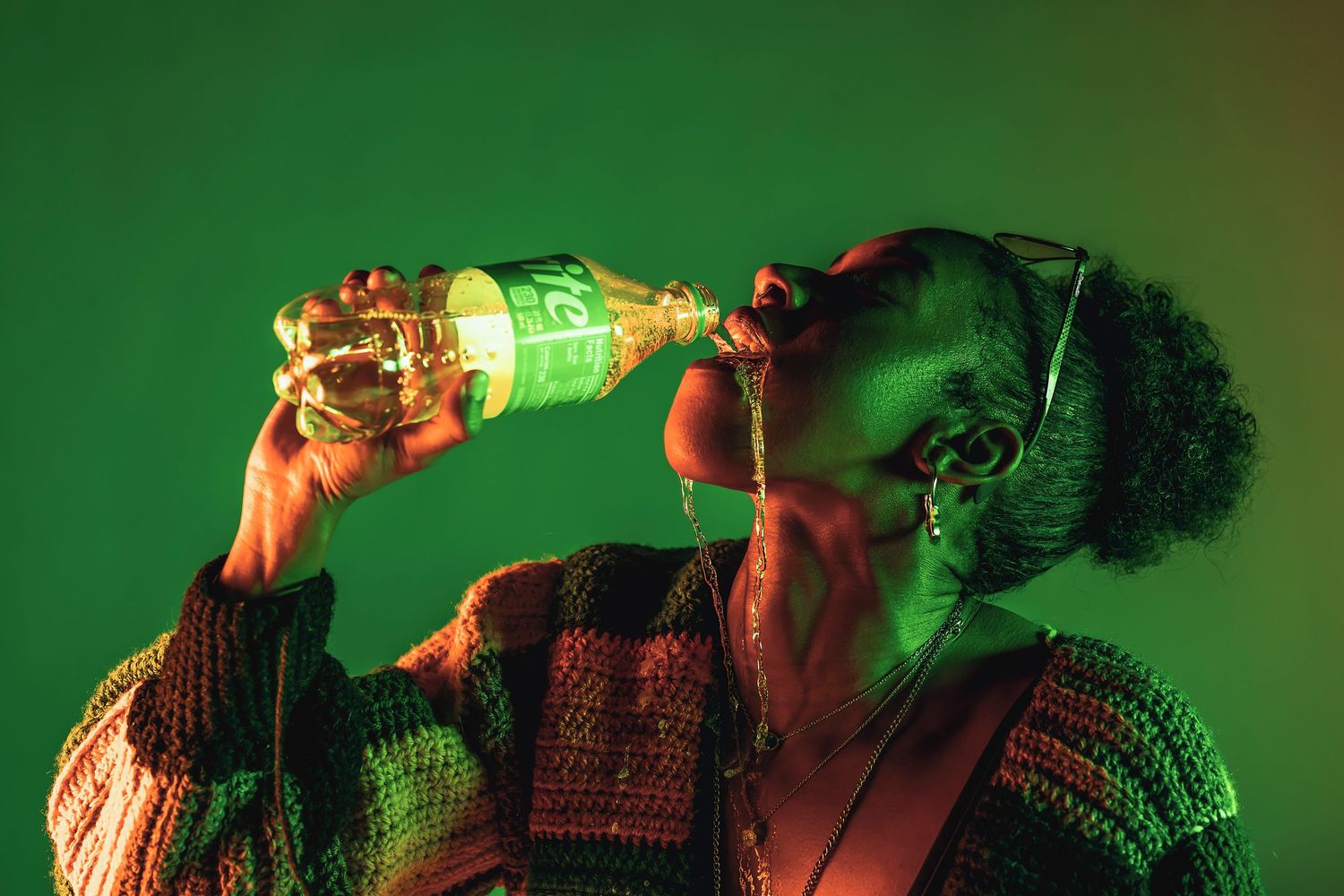 Person in knit sweater drinking from glowing green bottle in dramatic lighting.