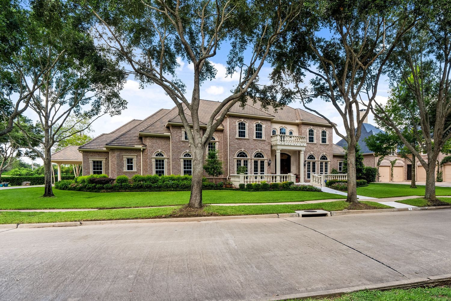 Large luxury mansion with two-story columns and mature oak trees on landscaped suburban street.