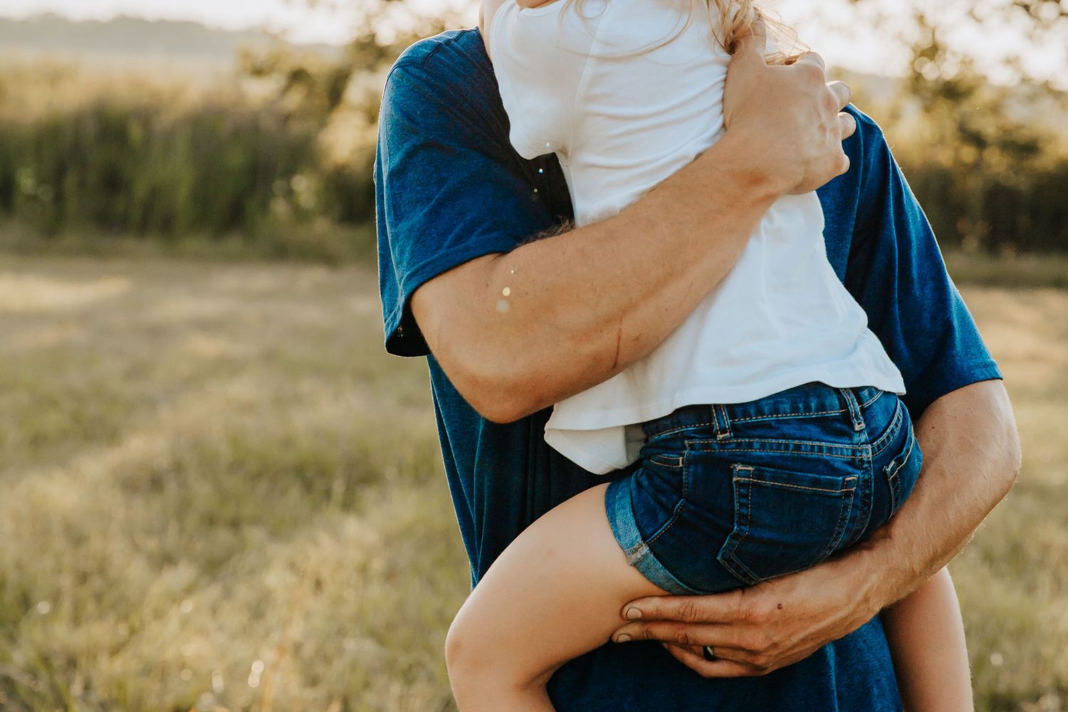 Close-up shot of someone holding a small child against blue denim in an outdoor setting.