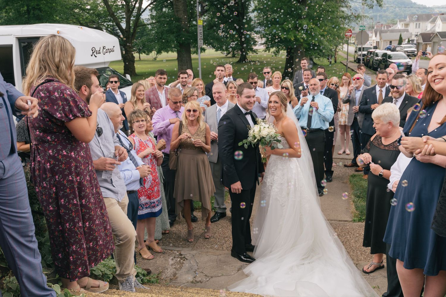 Wedding guests gather outdoors to celebrate as newlyweds exit their ceremony at an outdoor venue.