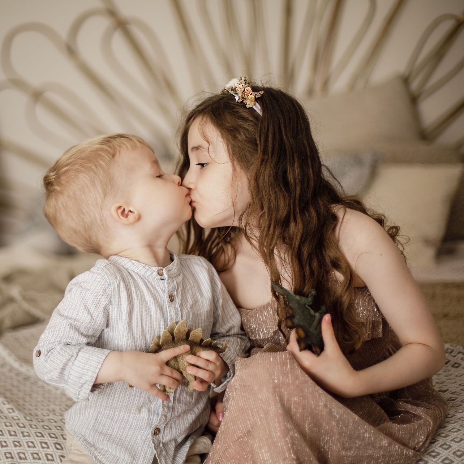 Brother and sister holding with dinosaurs while they kiss.