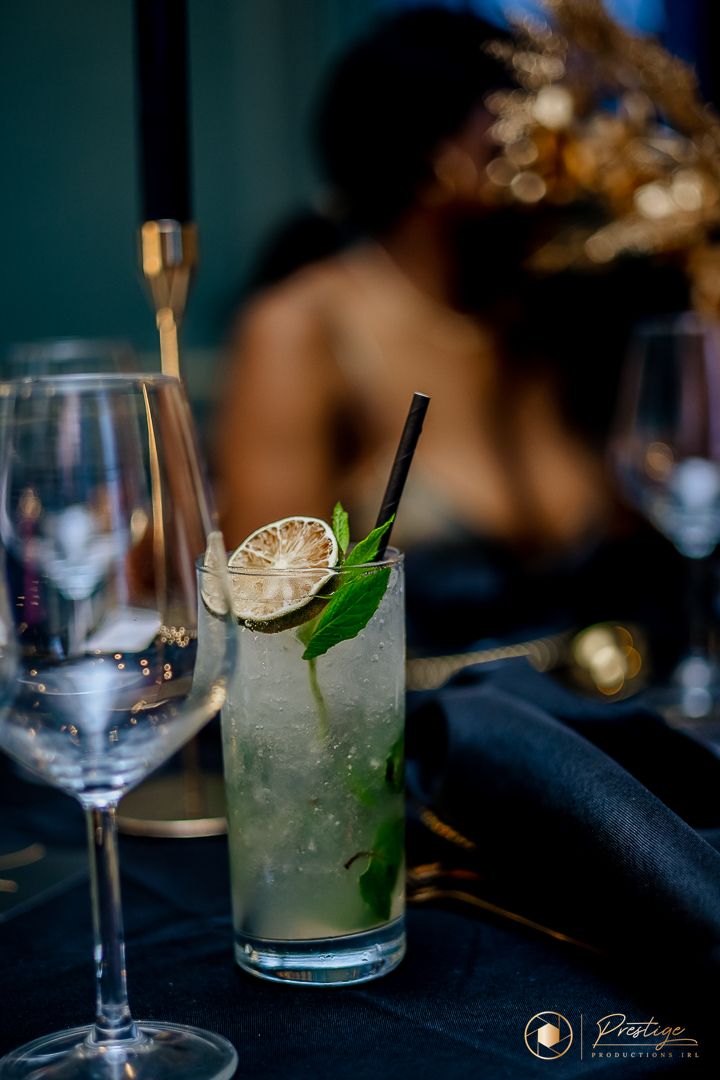 Refreshing cocktail with lime and mint garnish served in a highball glass with wine glasses nearby.