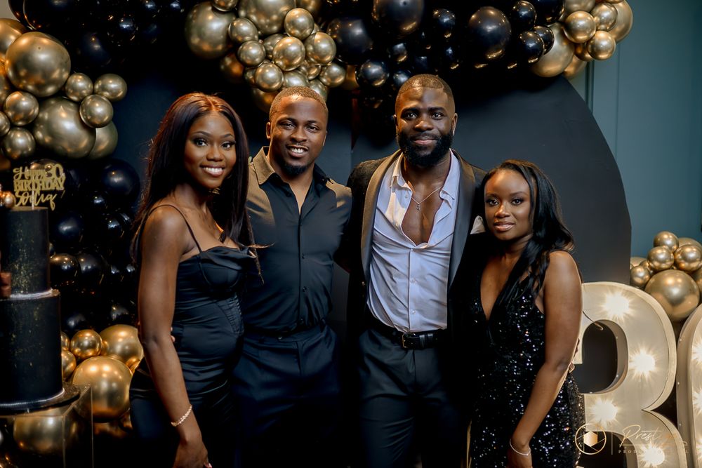 Formal party guests posed against black and gold balloon backdrop.