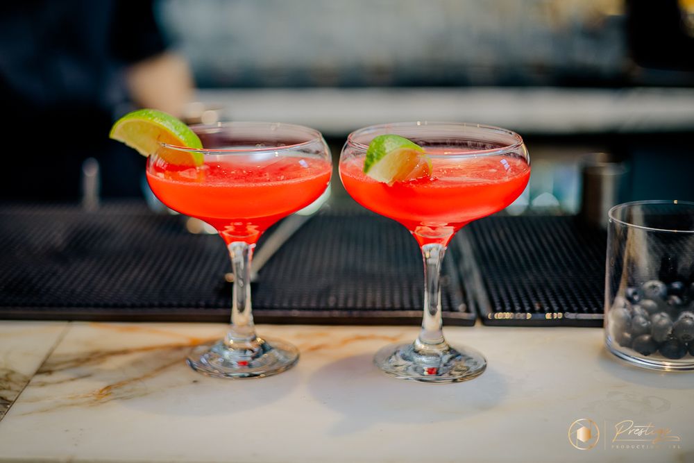 Two red cocktails garnished with lime slices served in coupe glasses on a bar counter.