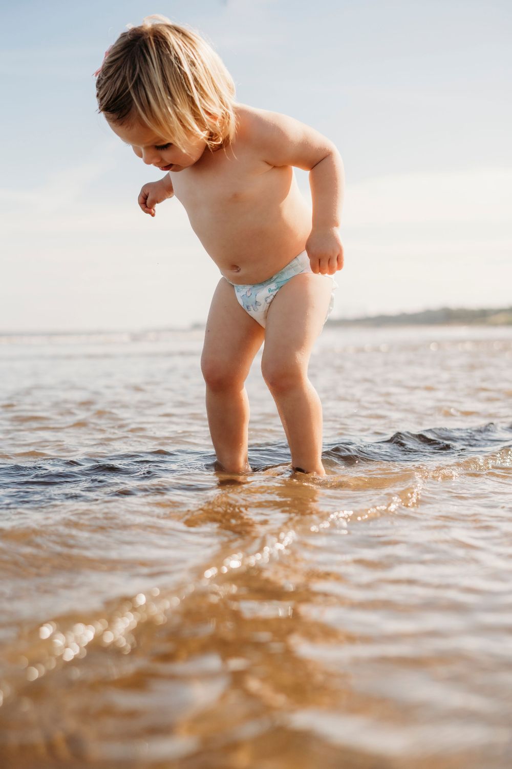 Toddler splashing and playing in shallow ocean waves during golden hour.
