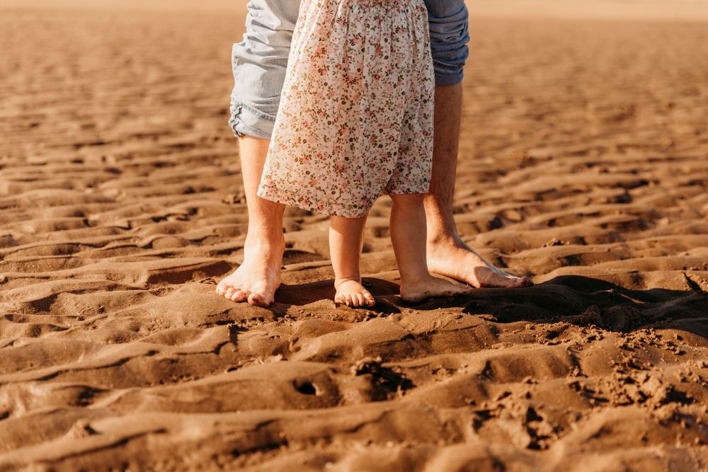 Bare feet standing together on textured sand during beach photoshoot.