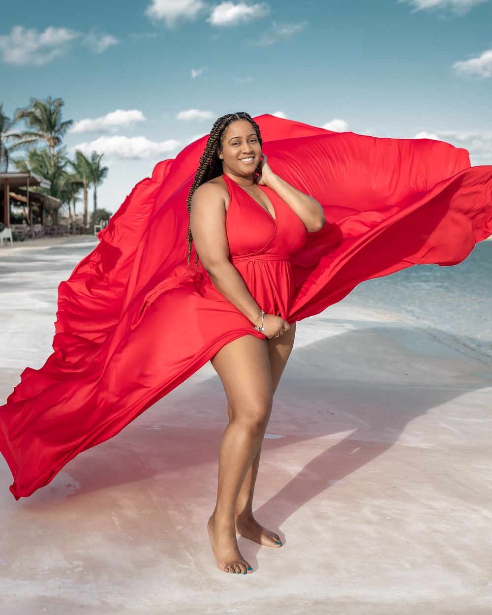 Red flowing dress catches ocean breeze during beach photoshoot.