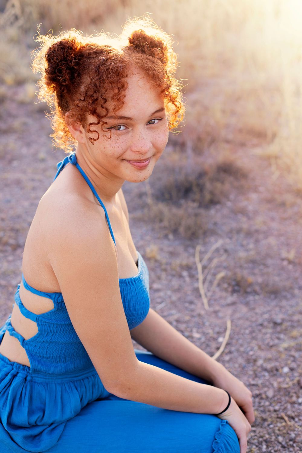 Person in bright blue dress poses against desert backdrop in warm sunlight.